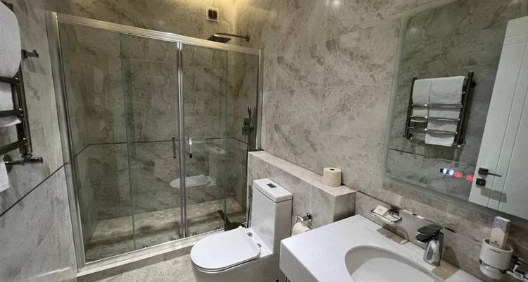 Modernes Hotelbadezimmer mit ebenerdiger Glasdusche, Marmorfliesen und sauberen weißen Armaturen.