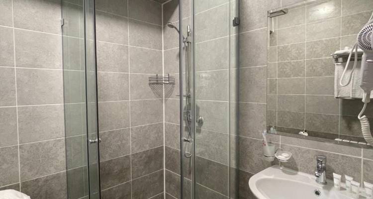 Einfaches gefliestes Hotelbadezimmer mit Glasduschkabine und kleinem Waschbeckenunterschrank.