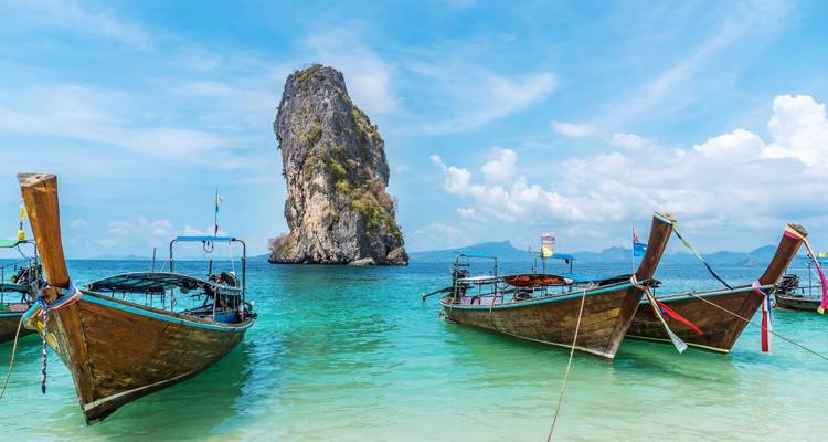 Les bateaux traditionnels à longue queue ancrés dans des eaux turquoise face à une haute île karstique en calcaire sous un ciel bleu