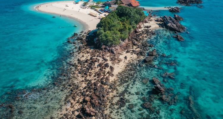 Vue aérienne par drone d'une île rocheuse avec une petite station balnéaire entourée d'eau bleu clair et de récifs coralliens