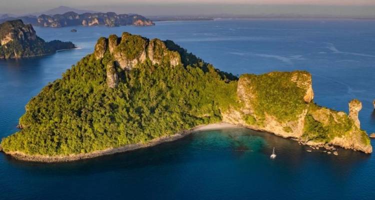 Île verdoyante s'élevant abruptement de la mer bleu profond à l'heure dorée avec un arrière-plan de formations karstiques lointaines