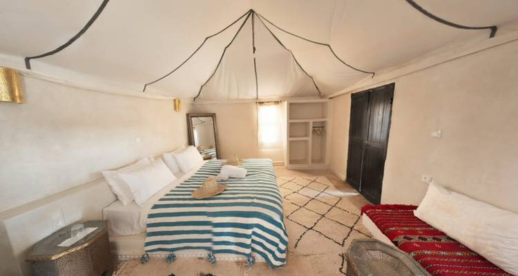 Suite de tienda de campaña estilosa en el desierto con camas gemelas, mantas rayadas y luz natural filtrándose a través del techo de lona.