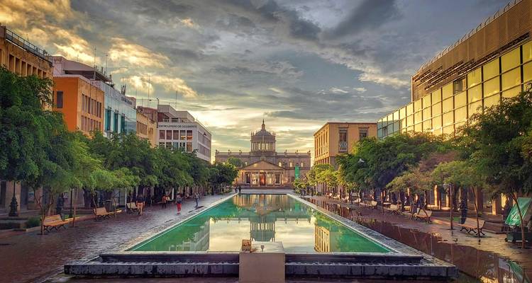 Gran bulevar con un estanque reflectante que conduce a un edificio histórico con cúpula al atardecer dramático