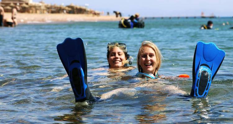 Zwei Schnorchler lächeln im klaren Wasser des Roten Meeres, blaue Flossen erhoben, mit entfernten Tauchern im Hintergrund.