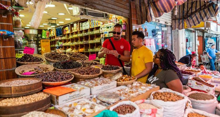 Los viajeros prueban cestas de frutas secas y nueces en un puesto de mercado de Oriente Medio muy concurrido.
