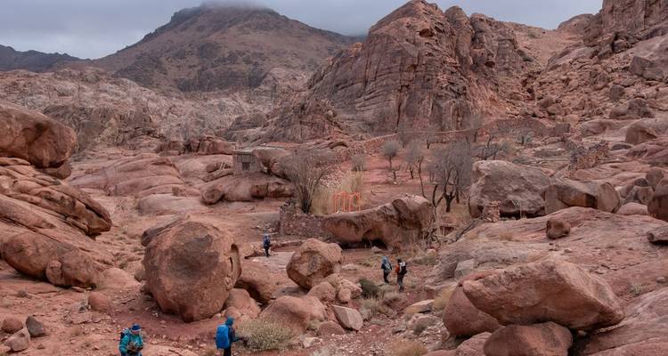 Los excursionistas atraviesan un valle rocoso y azotado por el viento del Monte Sinaí bajo cielos nublados.