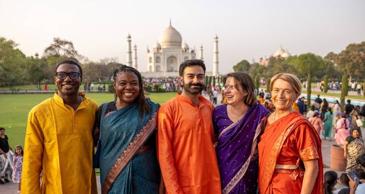 Un groupe coloré de visiteurs vêtus de costumes traditionnels sourit devant le dôme en marbre blanc du Taj Mahal.