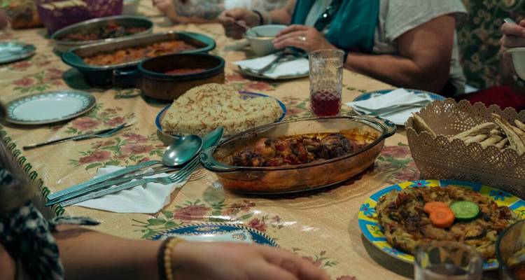 Une table de style familial est dressée avec des plats égyptiens maison, du pain plat et des assiettes colorées attendant les convives.