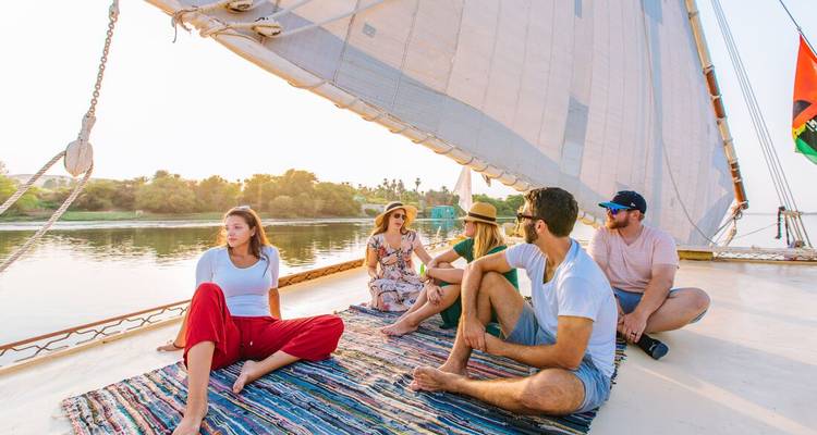 Les voyageurs se détendent sur des tapis colorés sous la voile d'une felouque glissant paisiblement le long du Nil.