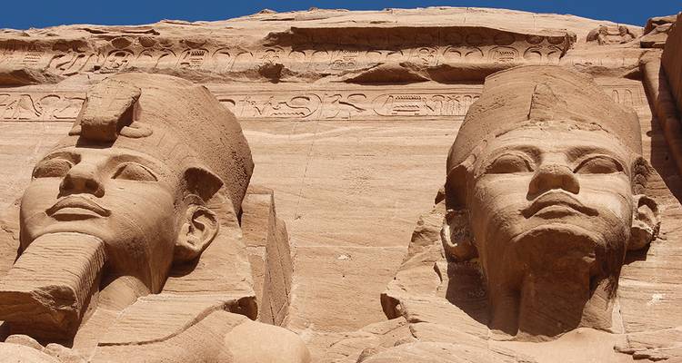 Gros plan en contre-plongée de deux statues monumentales de pharaon en grès à Abu Simbel encadrées par un ciel bleu profond.