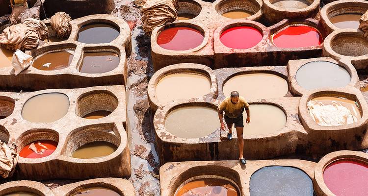 Vue aérienne des bacs de teinture multicolores dans la tannerie ancienne avec un ouvrier marchant entre les fosses.