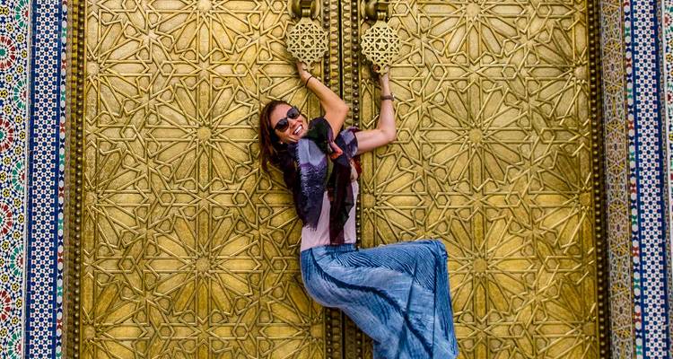 Voyageur joyeux s'accrochant avec malice aux portes dorées ornementées du Palais Royal à Fès.
