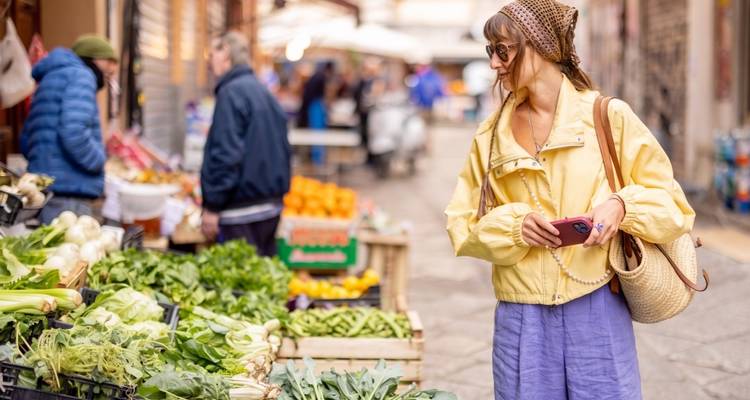 Young woman shopping for fresh produce at an open-air Italian market.