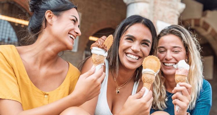 Three friends laughing while eating ice-cream cones outside an Italian piazza.