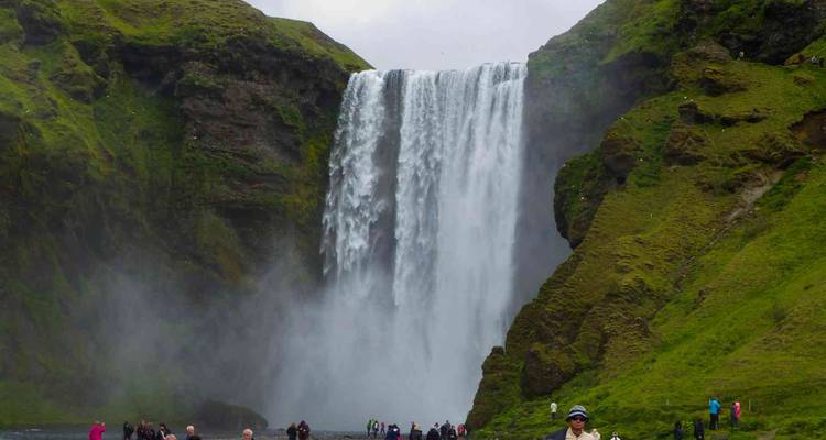 Visitors gathered at the misty base of Skogafoss waterfall cascading over green cliffs.