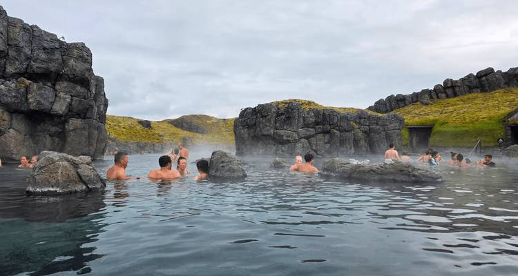 Travellers relaxing in a natural hot spring surrounded by volcanic rock and steam.