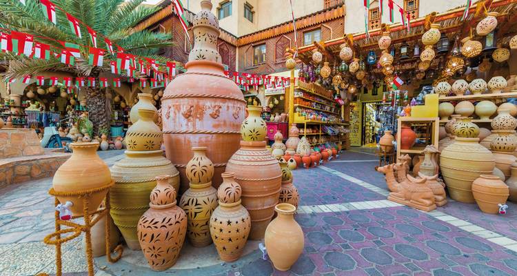 Farbenfroher Töpfermarkt mit Stapeln traditioneller Tonkrüge, omanische Flaggen über Kopf und Laternen zum Verkauf.
