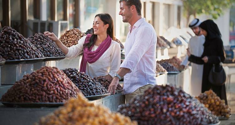 Lachendes Paar wählt Datteln an einem Marktstand im Freien aus, der mit verschiedenen Dattelsorgen gestapelt ist.