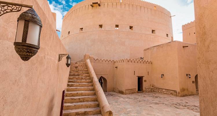 Steintreppe und Innenhof in einem historischen omanischen Fort mit abgerundeten Turmwänden.