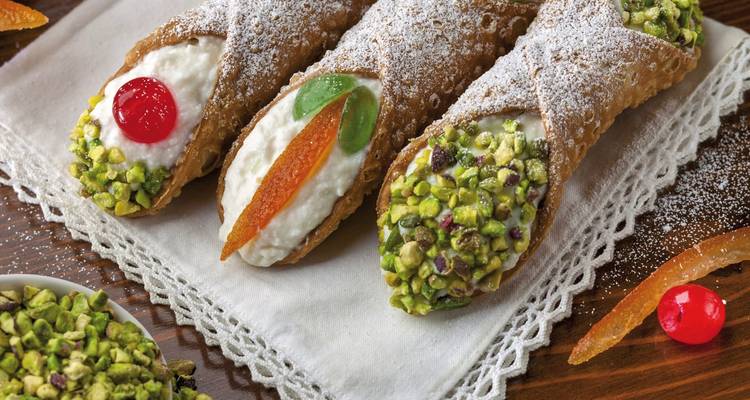 Trois cannoli siciliens garnis de ricotta et décorés de pistaches, de fruits confits et de sucre glace.