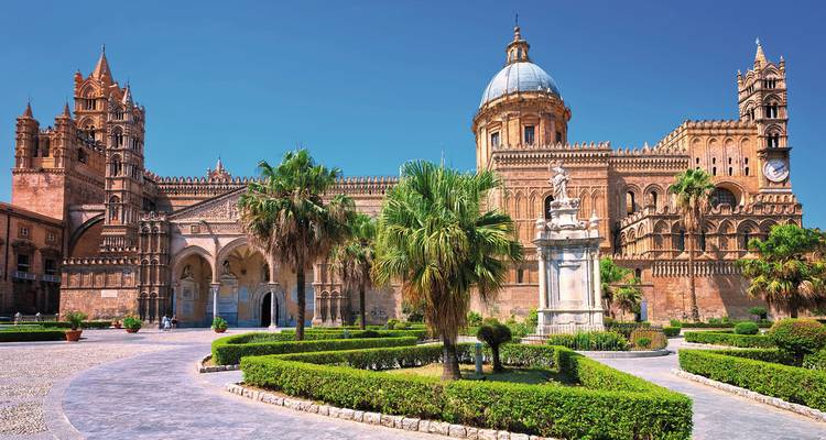 Façade impressionnante de la Cathédrale de Palerme avec des jardins bordés de palmiers sous un ciel bleu éclatant.
