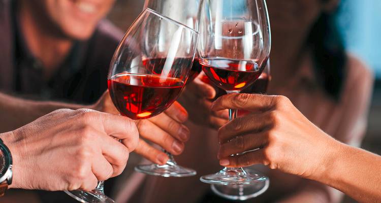 Gros plan d'amis qui font tinter leurs verres de vin rouge lors d'un toast de célébration.