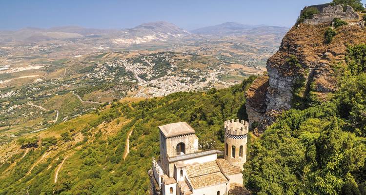 Château perché dominant une vaste vallée sicilienne couverte de terres agricoles verdoyantes et de montagnes lointaines.