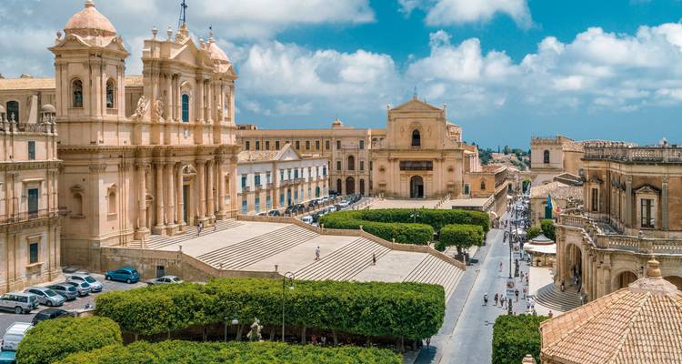 Vue surélevée de la place de la cathédrale de Noto avec ses bâtiments baroques et ses rues bordées d'arbres par un jour partiellement nuageux.