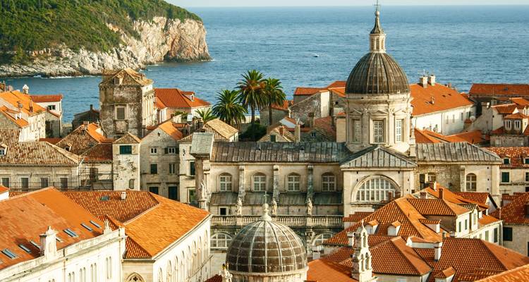 Iglesias de piedra histórica y techos de barro cocido de Dubrovnik con el mar Adriático de fondo.