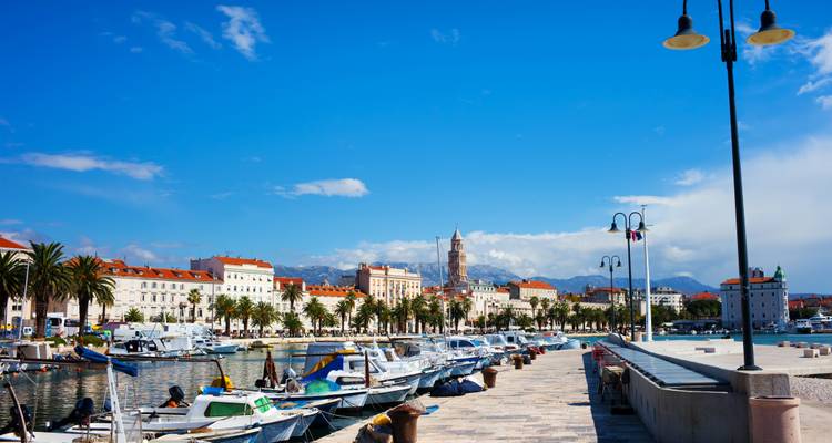 Paseo marítimo de Split lleno de barcos, palmeras y la torre del Palacio de Diocleciano.