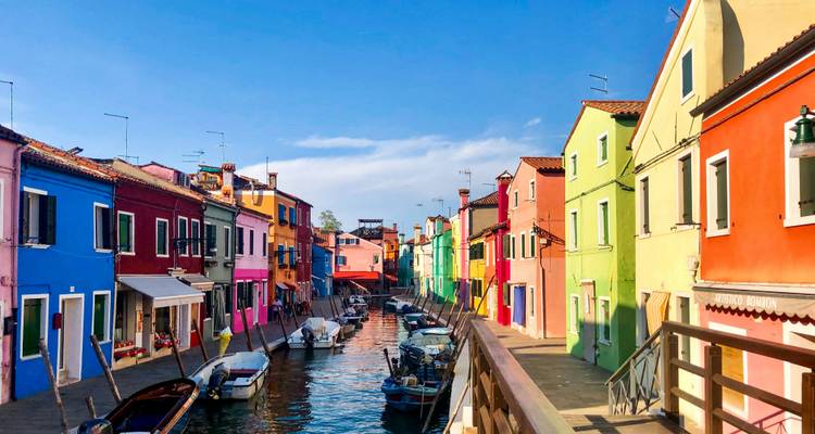 Casas pintadas con colores brillantes bordeando un estrecho canal con pequeños botes en la isla de Burano.