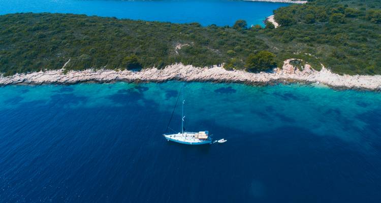 Velero anclado en una bahía turquesa cristalina junto a la costa de una isla boscosa.
