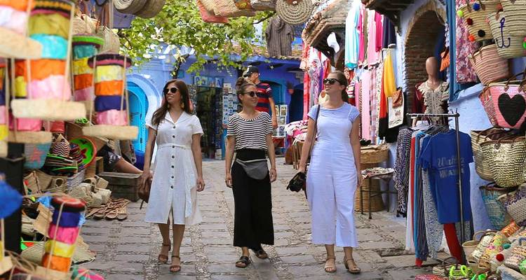 Trois femmes se promènent dans un souk coloré à Chefchaouen bordé de paniers tissés et de textiles.