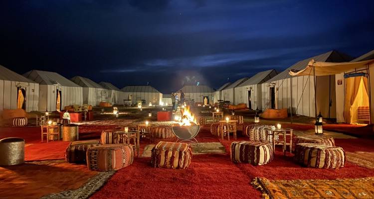 Camp désertique nocturne avec foyer et tapis berbères entre les tentes en toile
