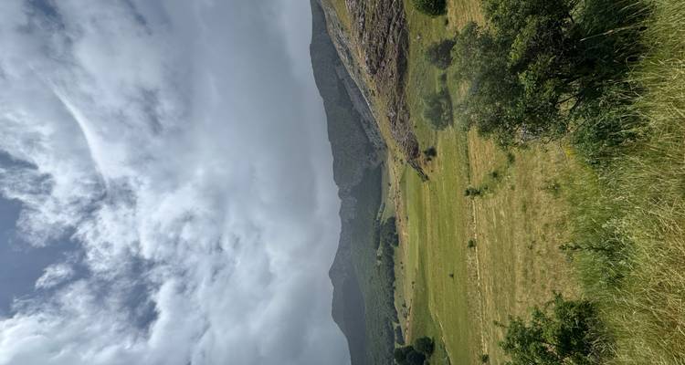 Vaste plaine herbacée avec des collines ondulantes et des formations nuageuses spectaculaires au-dessus.