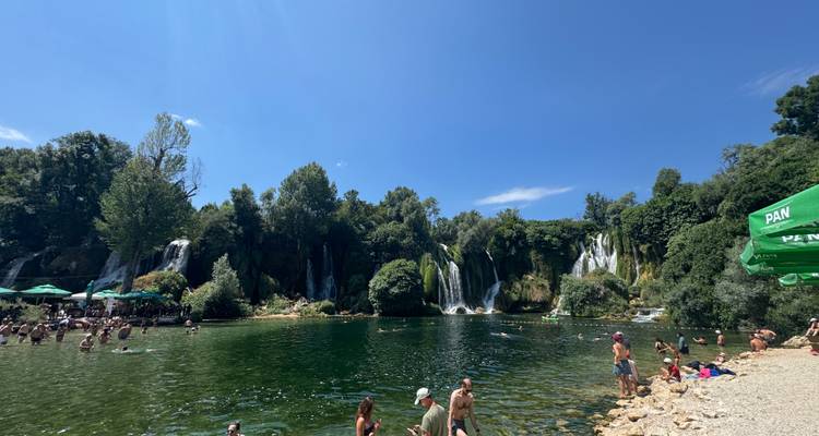 Grand bassin naturel avec des baigneurs profitant de la base des chutes d'eau en cascade multiple de Kravice par une journée ensoleillée.