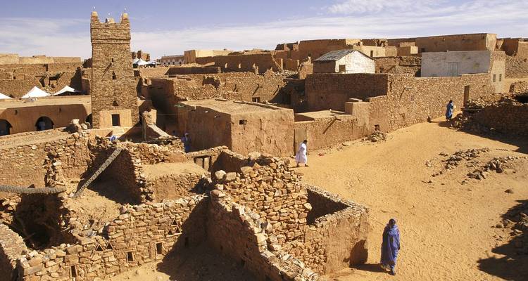 Sand-colored stone houses and ancient mosque of Chinguetti old town against blue sky.