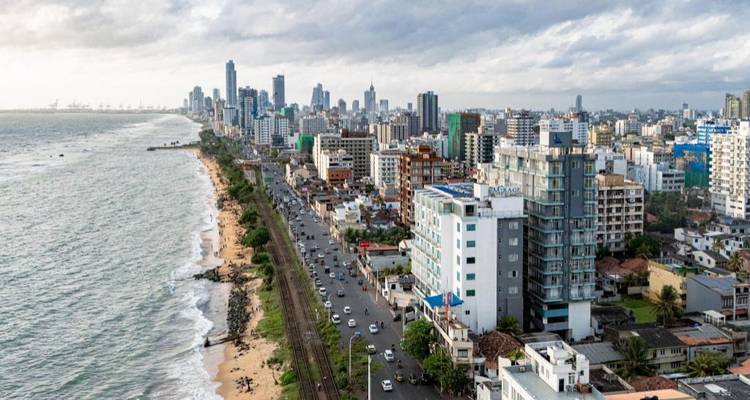 Vista aérea de la costa de Colombo con un moderno horizonte de ciudad, una carretera concurrida y una línea ferroviaria a lo largo de la playa.
