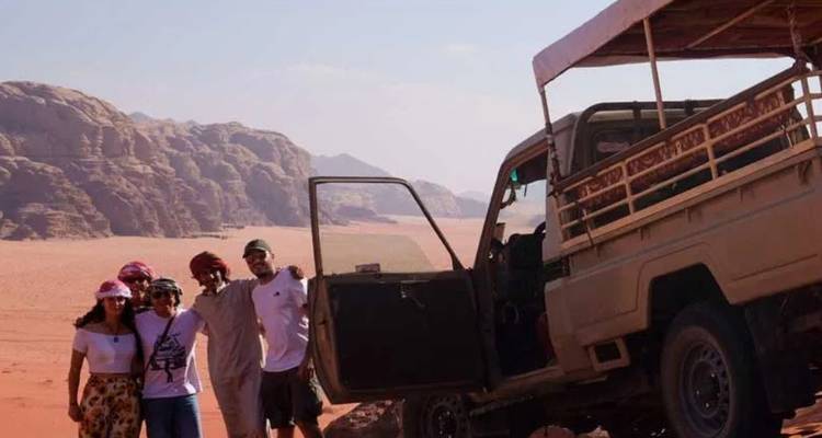 Group posing beside a 4x4 truck amid the dramatic red dunes and rock formations of Wadi Rum.