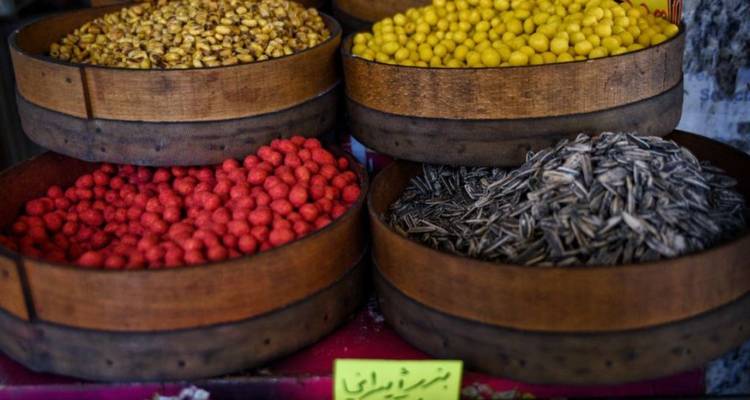 Close-up of colorful roasted nuts and seeds neatly displayed in wooden bowls at a market stall.