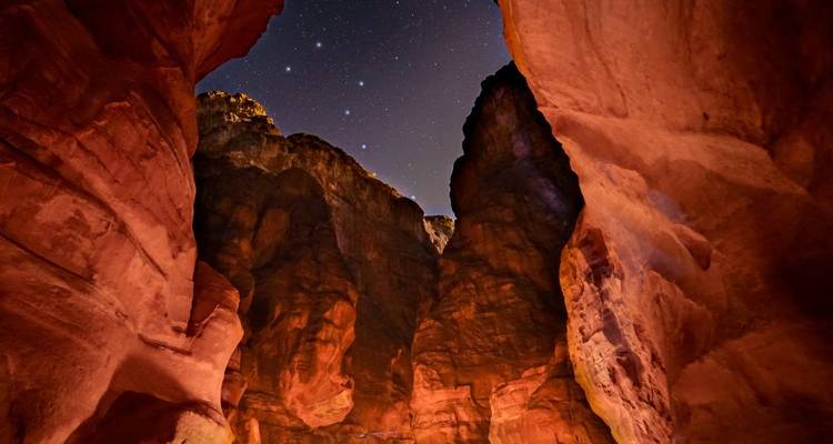 Night view of Petra’s narrow sandstone canyon walls under a star-filled sky.