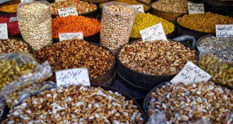 Variety of nuts and legumes arranged in sacks and bowls at a bustling Middle Eastern market.