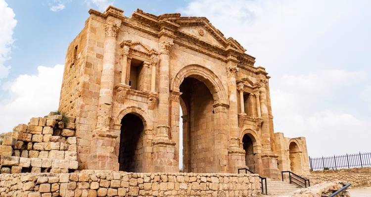 Hadrian’s Arch of Jerash rising against a partly cloudy sky, photographed from a low angle.