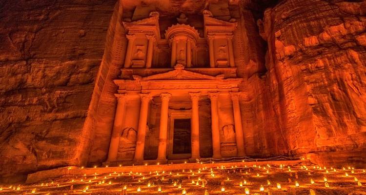 Petra Treasury illuminated by hundreds of candles during Petra by Night event, glowing red against rock walls.