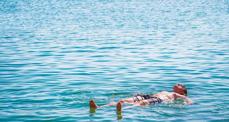Un hombre flotando sin esfuerzo sobre su espalda en las aguas azules y flotantes del Mar Muerto.