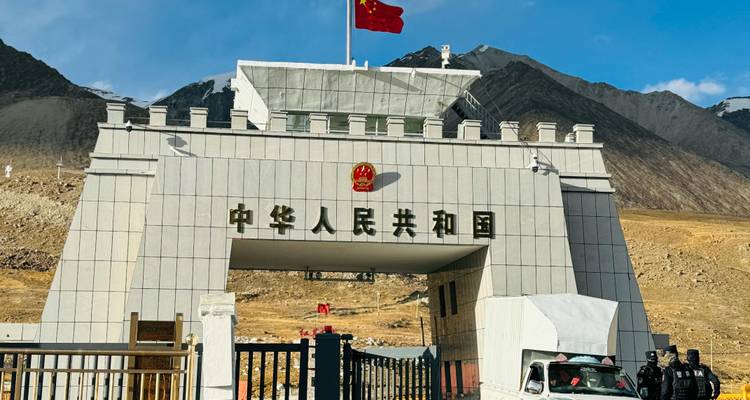 Granite border gate marked with Chinese characters and national flag stands against a backdrop of rugged mountains.