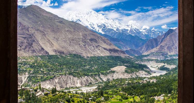 Framed by a wooden window, a lush valley and river lie beneath a towering snow-white peak in Hunza.
