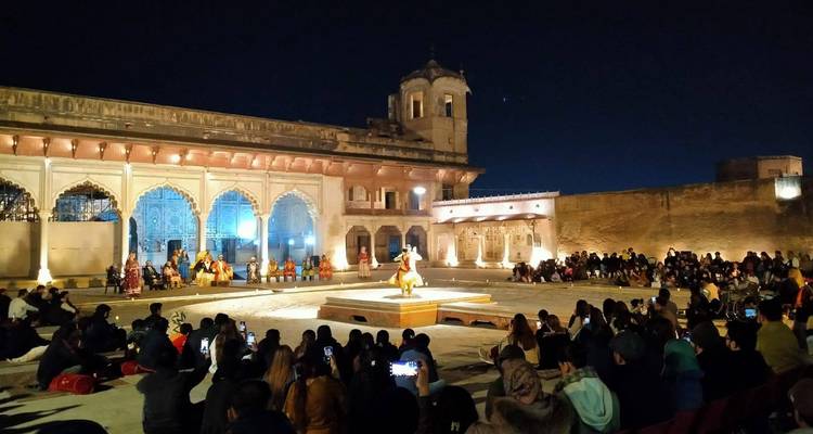 Représentation culturelle nocturne dans une cour historique avec le public assis autour de la scène illuminée