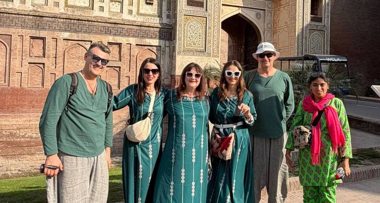 Groupe de touristes souriants posant dans des tenues assorties de couleur bleu-vert avant une porte historique ornée