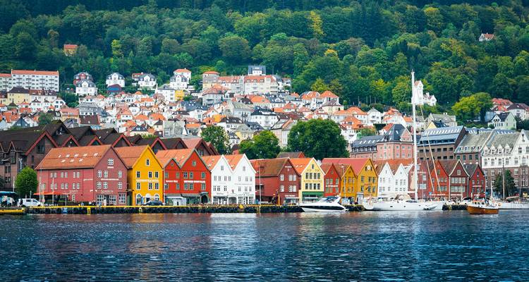 Kleurrijke houten Bryggen-pakhuizen voeren de rij langs Bergens haven met beboste heuvels erachter.